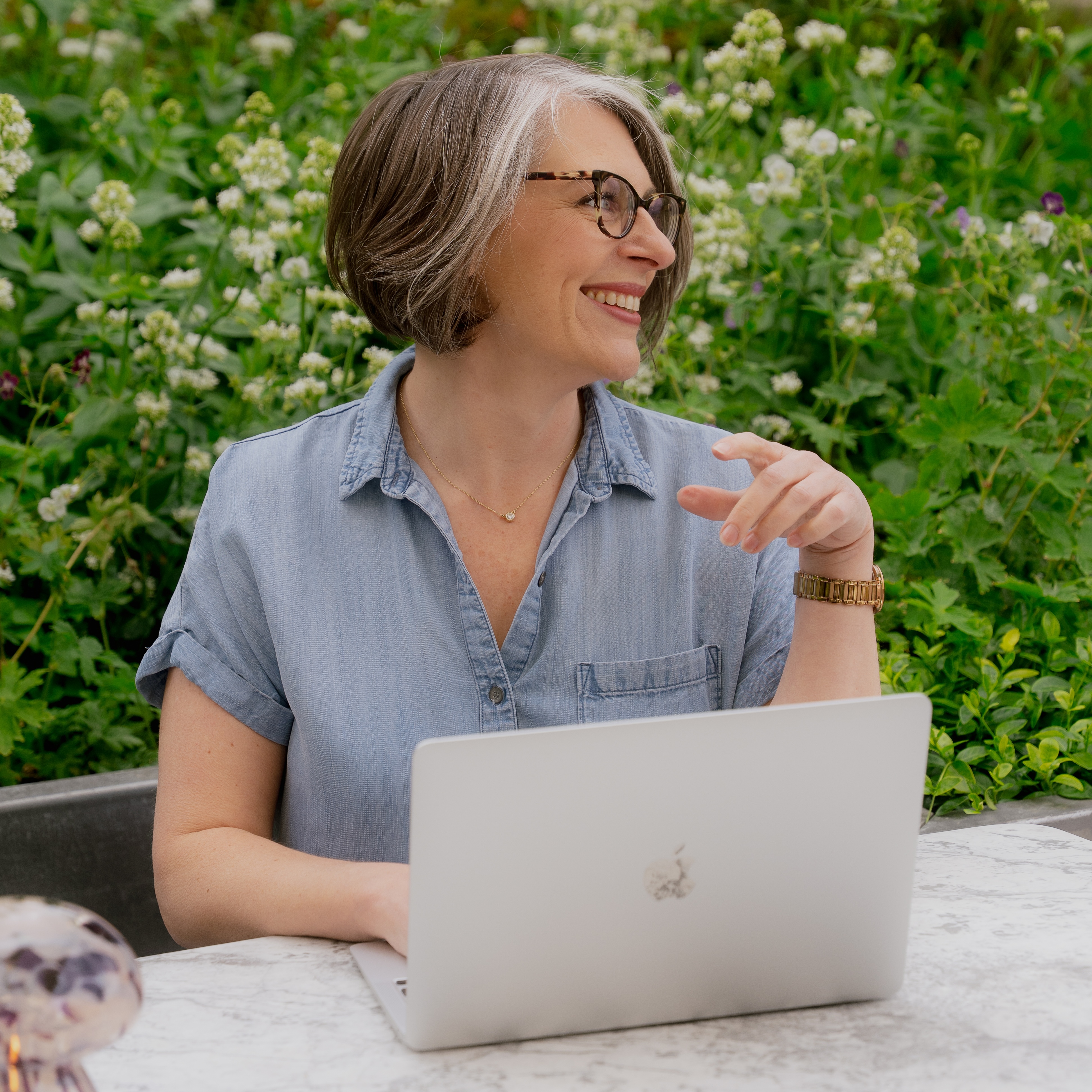 A woman sitting in a garden with a laptop